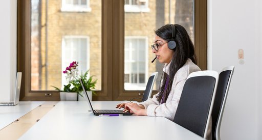 Woman talking on the phone with headphones and computer.