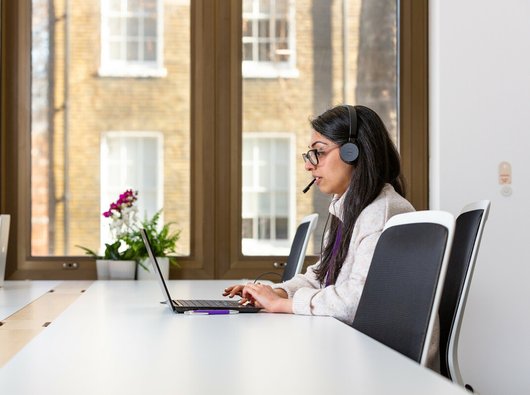 Woman talking on the phone with headphones and computer.