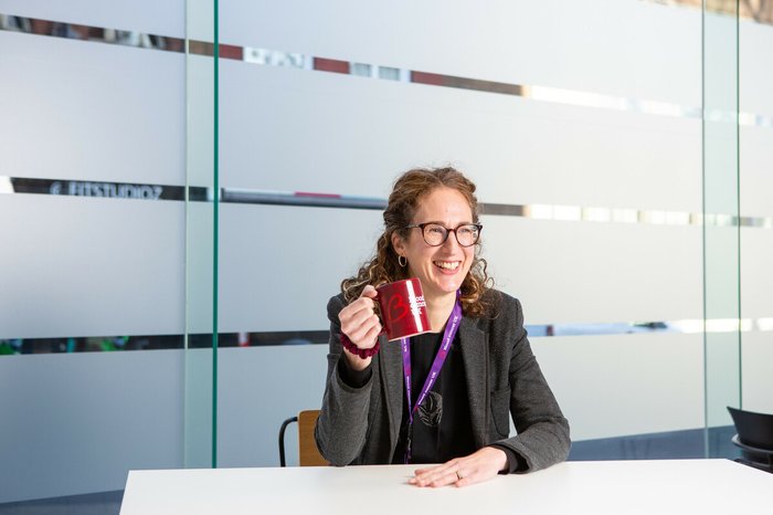 Blood Cancer UK's CEO, Helen Rowntree, holding a Blood Cancer UK coffee mug in the office and smiling.
