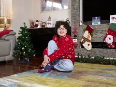 Alyssa sitting at home amongst Christmas decorations, smiling in her Christmas jumper.