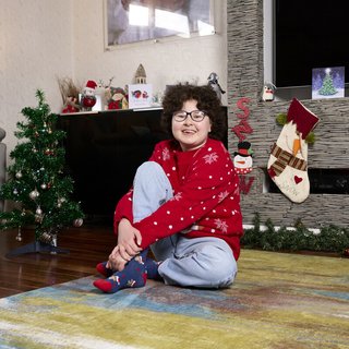 Alyssa sitting at home amongst Christmas decorations, smiling in her Christmas jumper.