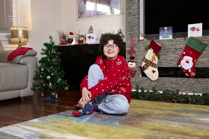 Alyssa sitting at home amongst Christmas decorations, smiling in her Christmas jumper.