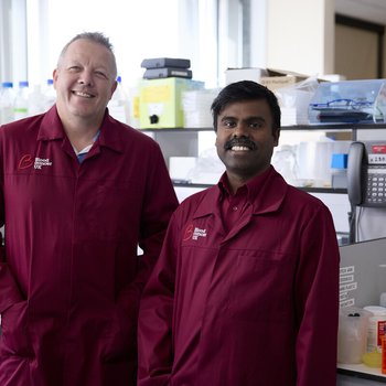 Two researchers wearing Blood Cancer UK lab coats, smiling in a lab.