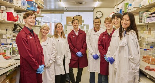 A group of Blood Cancer UK researchers all standing together in a lab, wearing their lab coats and smiling.
