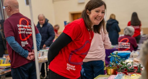 A woman wearing a Blood Cancer UK t-shirt at a fundraiser, smiling.