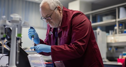 Researcher wearing a branded Blood Cancer UK burgundy lab coat, using equipment in the lab