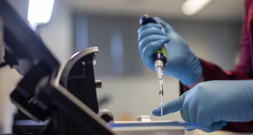 Close up of a researcher's hand and a pipette in the lab.