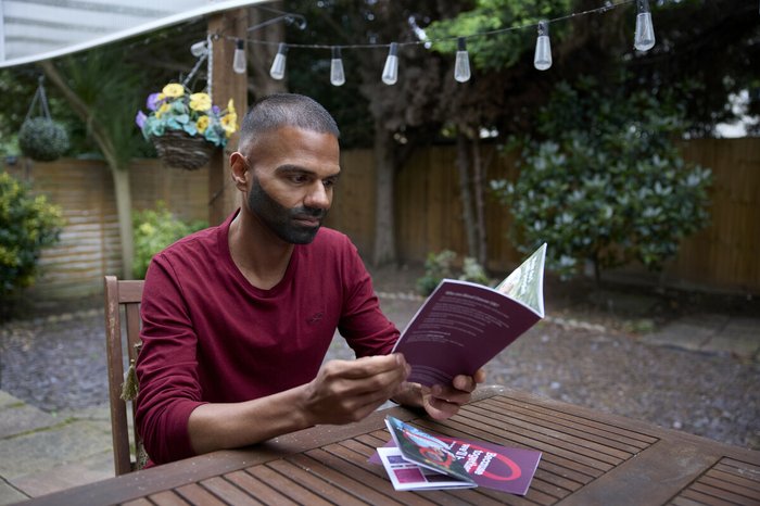 A man sitting in his garden at a table reading a booklet about blood cancer, looking focused but although his thoughts are elsewhere.