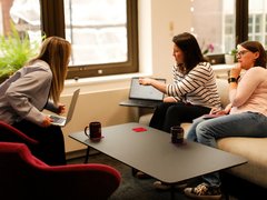 Three Blood Cancer UK members of staff chatting and talking by their computers in the office.