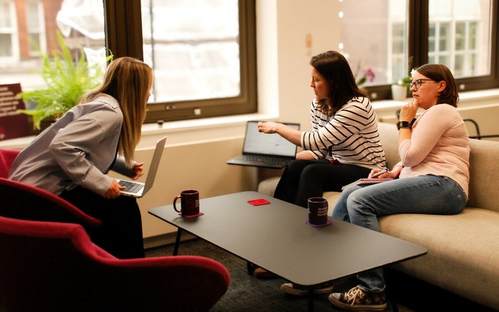 Three Blood Cancer UK members of staff chatting and talking by their computers in the office.