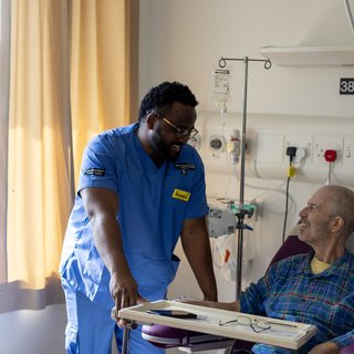 A black healthcare professional giving a caring look to a patient in his hospital bed.