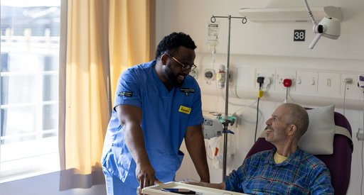 A black healthcare professional giving a caring look to a patient in his hospital bed.