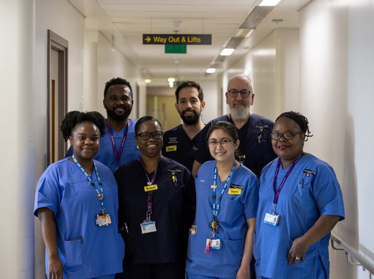 A diverse group of healthcare professionals looking at the camera, smiling, in a hospital hallway.