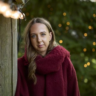 Molly outside in her winter jumper with Christmas lights around her.