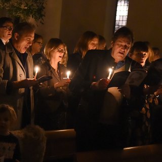 A group of people sing Christmas carols in a dark, candlelit room