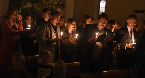 A group of people sing Christmas carols in a dark, candlelit room