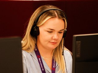 Rachel is sat looking at a laptop screen. She has a headset on and is speaking to someone on the phone.