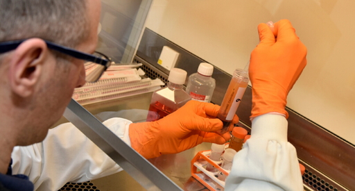 A researcher in a laboratory holding a vial filled with blood and a pipette