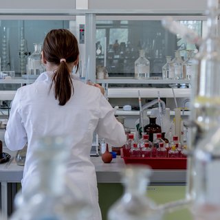 A researcher stands in a laboratory at a work bench surrounded by sample jars