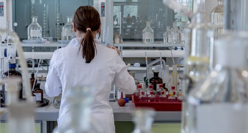 A researcher stands in a laboratory at a work bench surrounded by sample jars