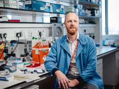 Dr Richard Dillon sat in the lab smiling wearing a light blue lab coat.