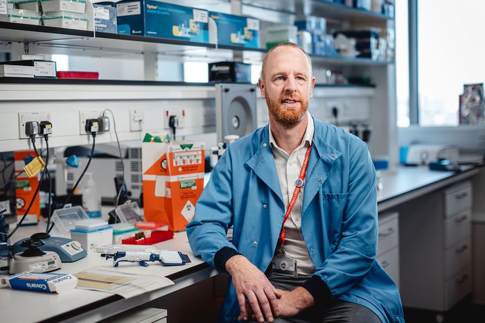 Dr Richard Dillon sat in the lab smiling wearing a light blue lab coat.