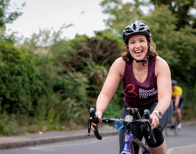 A woman smiles at the camera as she rides her bike through the countryside