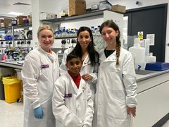 A group of people gathered together in the lab, wearing white lab coats, smiling at the camera