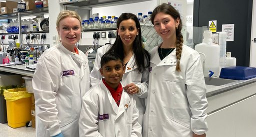 A group of people gathered together in the lab, wearing white lab coats, smiling at the camera