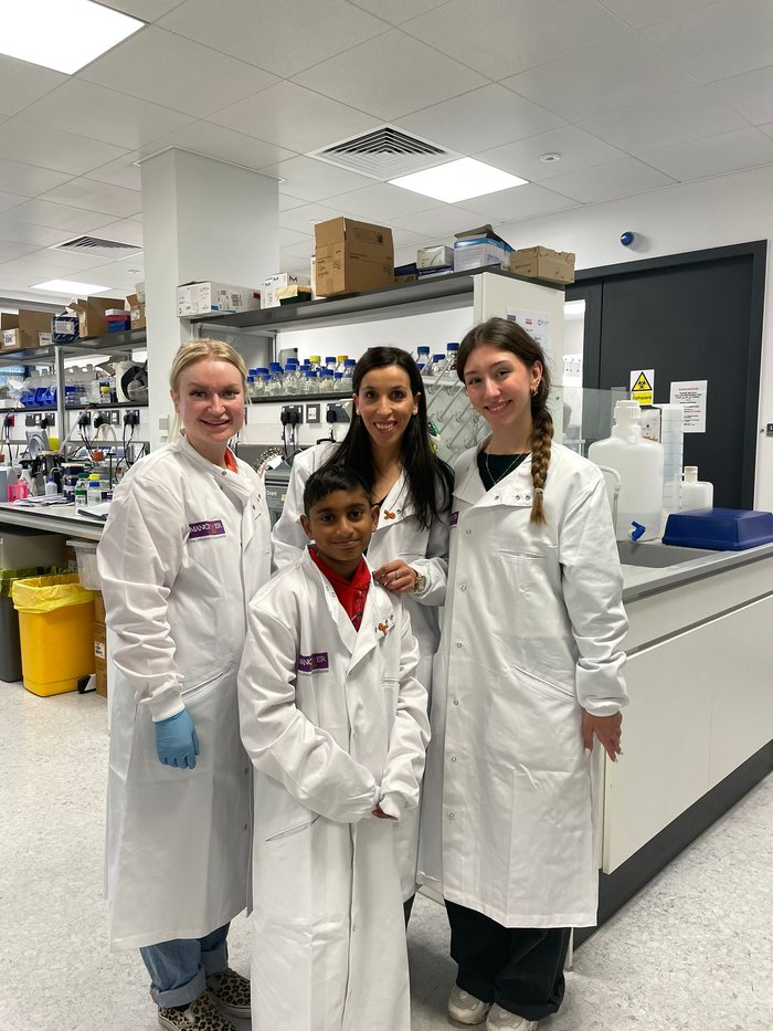 A group of people gathered together in the lab, wearing white lab coats, smiling at the camera