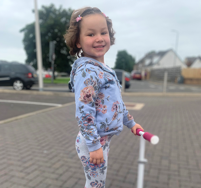 Five-year-old Mila Sneddon standing with her scooter smiling at the camera.