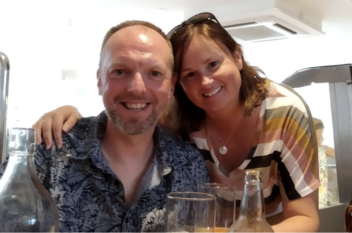 Jude with her arm around husband Nige, who was diagnosed with non-Hodgkin lymphoma, smiling at the camera.