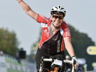 Sarah, who was diagnosed with chronic lymphocytic leukaemia (CLL), raising one arm whilst cycling and smiling at the camera.