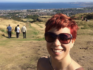 Emma, who was diagnosed with a myelodysplastic syndrome (MDS), smiling with sunglasses on up a hill with a city view in the background.