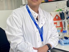 A lady stood in the lab wearing a white lab coat looking at the camera.