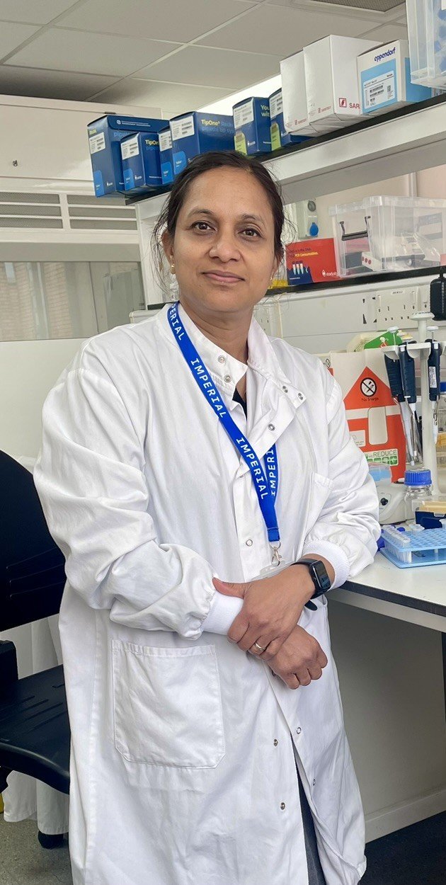 A lady stood in the lab wearing a white lab coat looking at the camera.