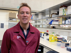Simon Thomas, stood in the lab wearing a red blood cancer UK lab coat.