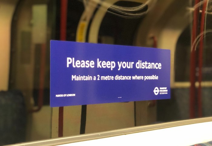 Transport for London sticker on the window of an underground train  displaying text to keep a 2 metre distance from others.
