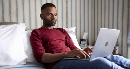 Man uses a laptop while sitting on a bed