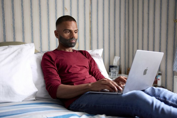 Man uses a laptop while sitting on a bed