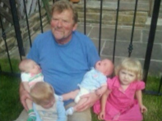 A man - Thomas - holds two small babies; another young boy sits between his knees, a young girl to his left.