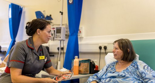 A nurse and a patient chat in the hospital. Theya are both sitting down.