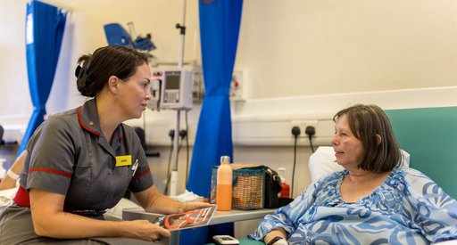 A nurse and a patient chat in the hospital. Theya are both sitting down.