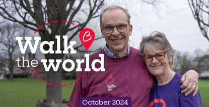 A male and a female with their arms round each other, smiling directly at the camera. Wearing Blood Cancer UK t-shirts with trees in the distance