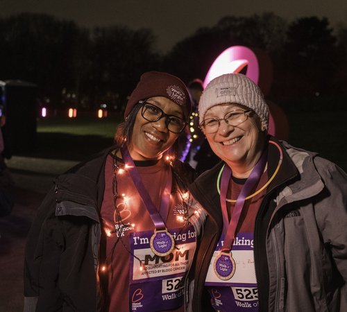 Two ladies wearing Walk of Light merchandise, with arms round each other smiling with lights around them