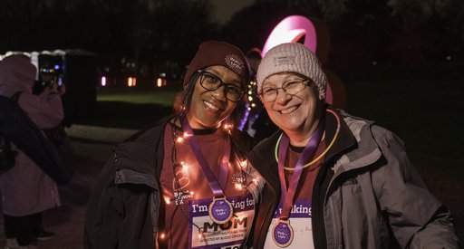 Two ladies wearing Walk of Light merchandise, with arms round each other smiling with lights around them
