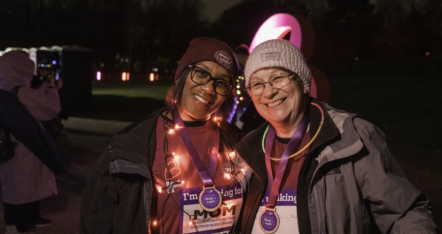Two ladies wearing Walk of Light merchandise, with arms round each other smiling with lights around them