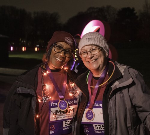 Two ladies wearing Walk of Light merchandise, with arms round each other smiling with lights around them