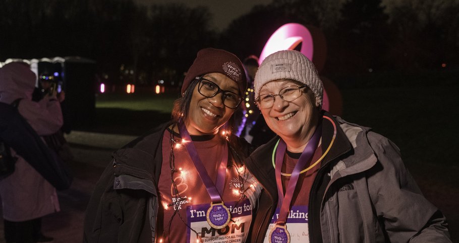 Two ladies wearing Walk of Light merchandise, with arms round each other smiling with lights around them