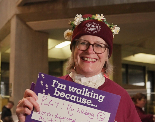 Lady wearing a Walk of Light beanie hat and holding a sign reading 'I'm walking because...'